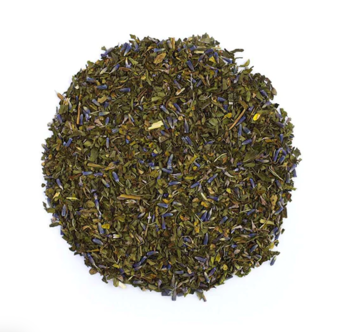 a top-down view of a round pile of loose leaf tea with purple lavender blossoms and black peppercorns. 