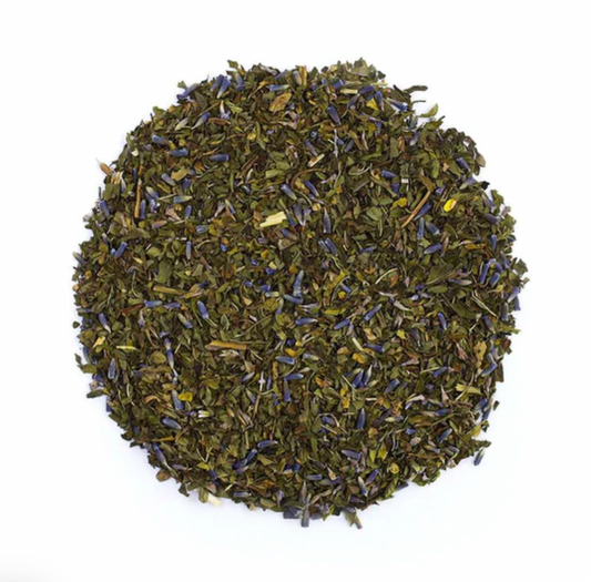 a top-down view of a round pile of loose leaf tea with purple lavender blossoms and black peppercorns. 